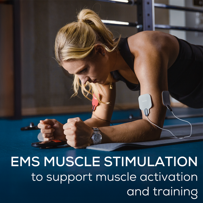 Woman exercising on a mat wearing 4 electrode pads on her arm connected to the TENS/EMS unit to support muscle stimulation and training.