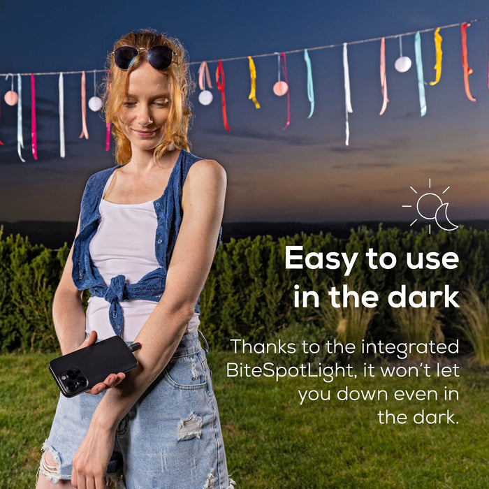 A woman standing outdoors at dusk highlighting the integrated BiteSpotLight feature. Text on the right reads 'Easy to use in the dark' and describes the integrated light.