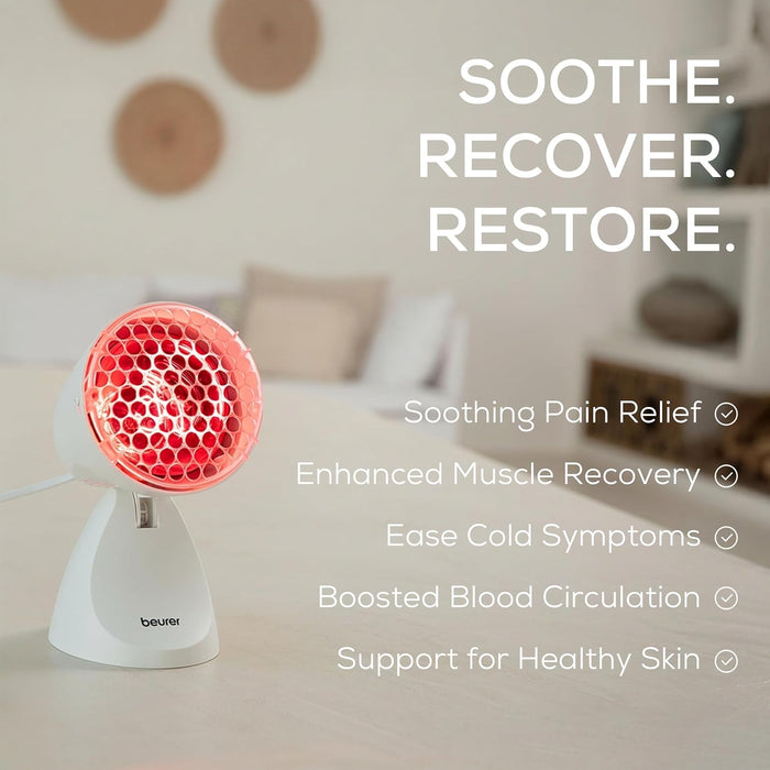 A white beurer infrared heat lamp with a glowing red-orange infrared light head, shown on a light surface with a blurred home interior background.