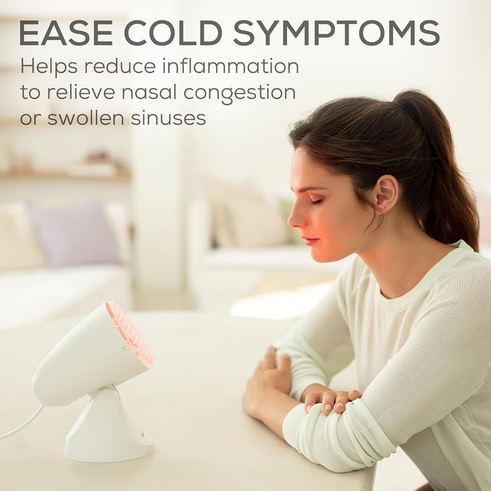 A woman sits at a table in a bright indoor setting, eyes closed sitting in front of IL11 using it to ease her cold symptoms.   